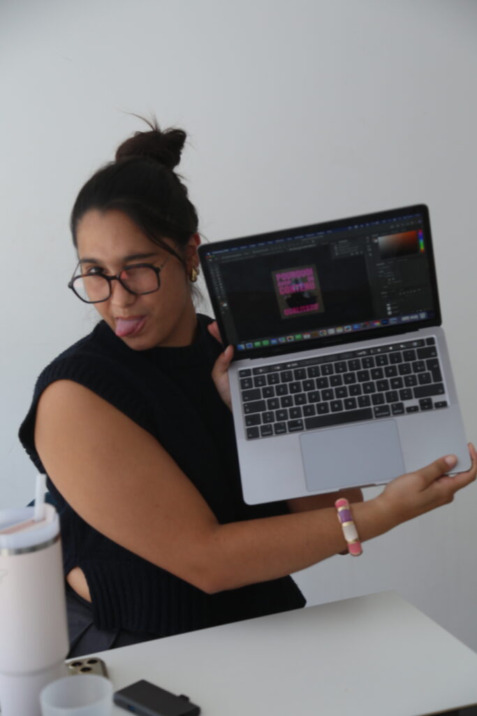 Une femme tient un ordinateur portable dans ses bras et pose face à l'objectif dans un espace de travail.